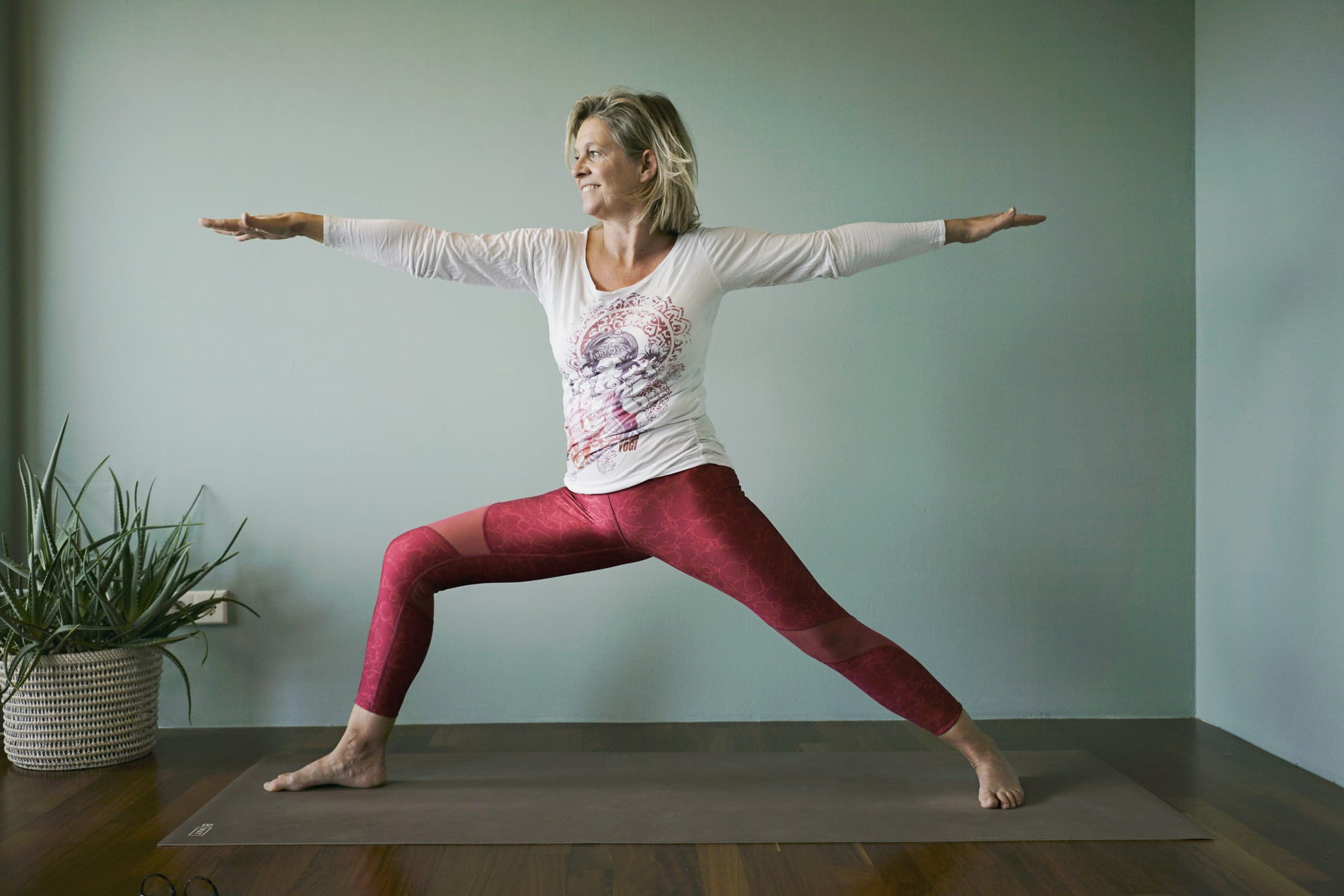 Yogalehrerin im Krieger II mit weit ausgebreiteten Armen