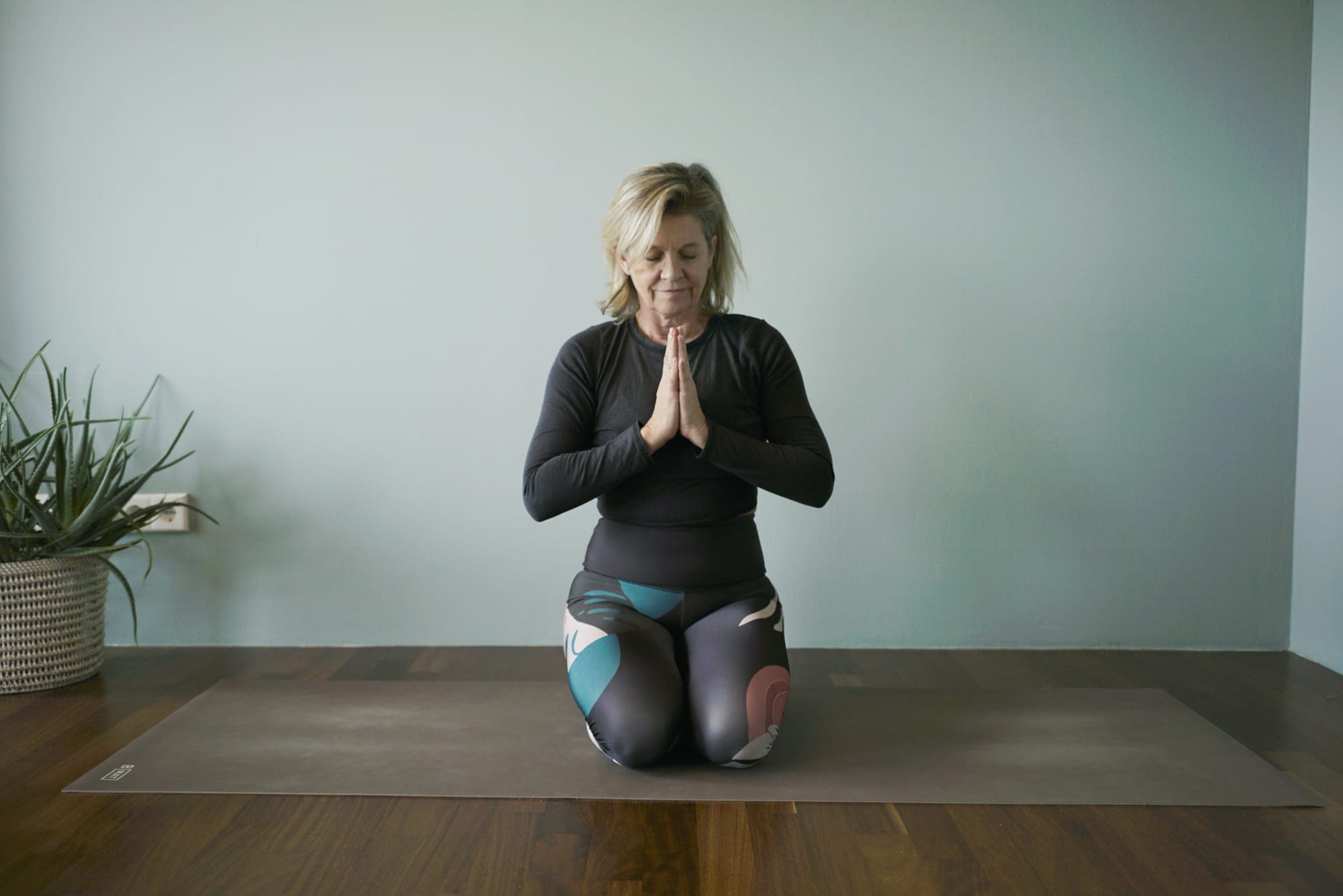 Yogalehrerin kniet auf der Matte, die Hände vor der Brust